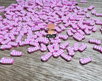 May include: A large quantity of pink and white candy cane shaped polymer clay charms. The charms are scattered on a wooden surface.