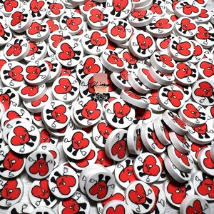 May include: A large pile of white ceramic heart-shaped charms with red and black painted details. Each heart has a frowning face with arms and legs.