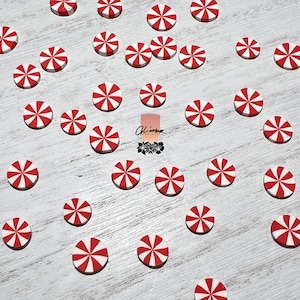 May include: A collection of red and white candy cane-shaped round embellishments. The embellishments are scattered on a white wooden surface.