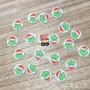 May include: A collection of 18 round white stickers with a green Grinch face wearing a red Santa hat.