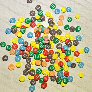 May include: A large group of colorful round candies with the letter "M" printed in white on each candy. The candies are in shades of red, orange, yellow, green, blue, and brown.