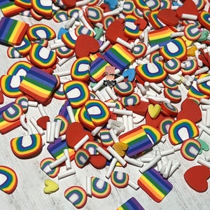 May include: A variety of rainbow-colored clay shapes, including hearts, rainbows, and squares, scattered on a white surface. The shapes are made of polymer clay and are perfect for adding a touch of whimsy to crafts and projects.