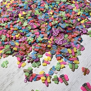 May include: A large pile of colorful butterfly-shaped charms. The charms are made of polymer clay and have a variety of colors and patterns.