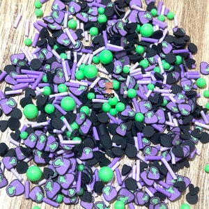 May include: A mix of purple, green, and black sprinkles in the shape of hearts, small circles, and long sticks. The sprinkles are perfect for decorating cakes, cupcakes, and other desserts.
