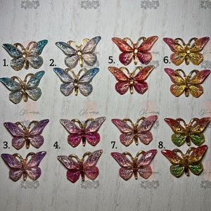 May include: Eight different butterfly-shaped resin embellishments with gold accents. The butterflies are in various colors, including blue, pink, red, and green.