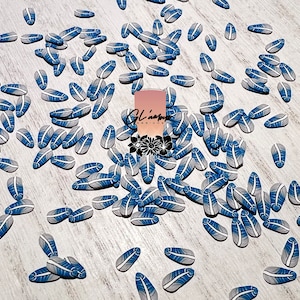 May include: A scattering of blue and white oval-shaped resin embellishments with a feather design. The embellishments are scattered on a light wood surface.