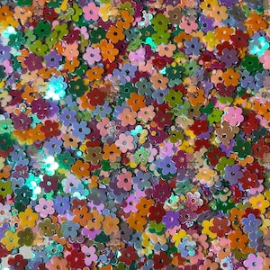 May include: A large assortment of colorful flower-shaped glitter. The glitter is iridescent and comes in a variety of colors, including red, orange, yellow, green, blue, purple, and pink.