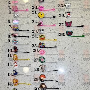 May include: A set of 38 colourful silicone charms with various designs, including cartoon characters, animals, and inspirational messages. The charms are attached to clear elastic bands, which can be used to hold hair or as keychains.