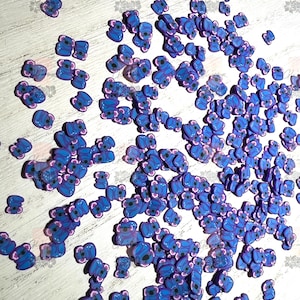 May include: A large quantity of blue and purple koala-shaped resin charms. The charms are scattered on a white surface.