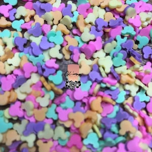 May include: A large quantity of small, colorful Mickey Mouse head-shaped sprinkles. The sprinkles are in shades of pink, purple, yellow, and green.