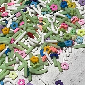 May include: A mix of green, white, and colorful flower-shaped sprinkles. The sprinkles are perfect for decorating cakes, cupcakes, and other desserts.
