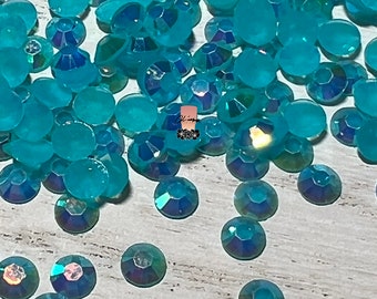 May include: A large quantity of turquoise blue iridescent rhinestones, scattered on a light wood surface.