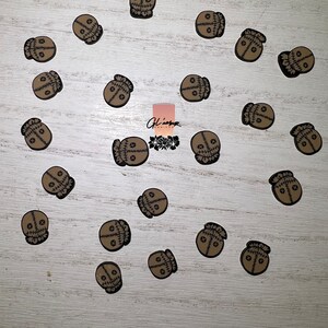 May include: A collection of 20 brown and black stitched fabric voodoo doll skull charms. The charms are arranged in a circle on a light wood surface.