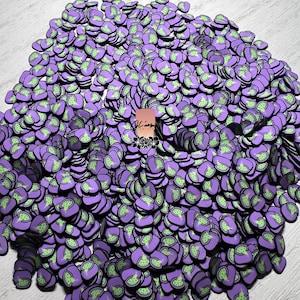May include: A large pile of purple and green heart-shaped resin charms. The charms have a green outline and a green design inside the heart.
