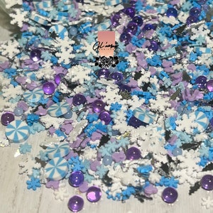May include: A mix of white, blue, and purple sprinkles in the shape of snowflakes, candy canes, and hearts. There are also small, round, purple beads.