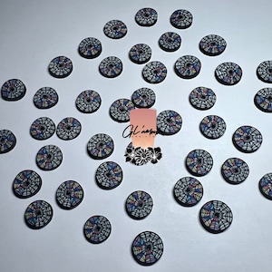 May include: A collection of small, round decorative buttons with a stained glass window design. Each button features a black border and a colorful, intricate pattern in shades of blue, yellow, pink, and green. The buttons are scattered on a white surface.