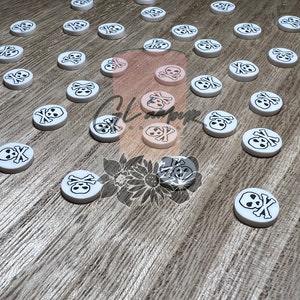 May include: A collection of white round skull and crossbones buttons. The buttons are scattered on a wooden surface.