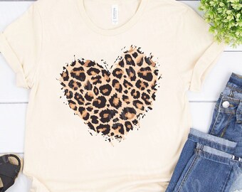 Peut inclure: Un t-shirt beige avec un grand motif de cœur imprimé léopard. Le cœur est souligné de noir et a un aspect vieilli.