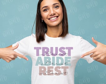 May include: A white t-shirt with the text "TRUST in Christ ABIDE in Christ REST in Christ" in purple, blue, and pink lettering.
