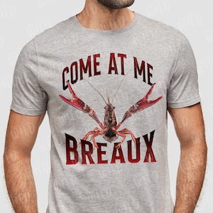 May include: A grey t-shirt with the text "COME AT ME BREAUX" in red. A red crawfish is pictured above the text.