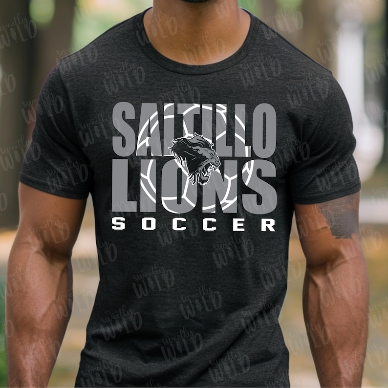 以下が含まれることがあります： 白とグレーの「SALTILLO LIONS SOCCER」の文字が入った濃いグレーのTシャツ。デザインにはライオンのグラフィックとサッカーボールのパターンが含まれています。このシャツはクルーネックです。
