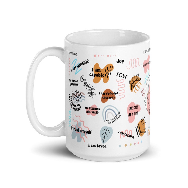 Puede incluir: Taza de cer&aacute;mica blanca con asa, decorada con afirmaciones coloridas y frases inspiradoras. La taza presenta frases como "Soy &uacute;nico", "Soy capaz" y "Soy amado", junto con formas y dise&ntilde;os abstractos.