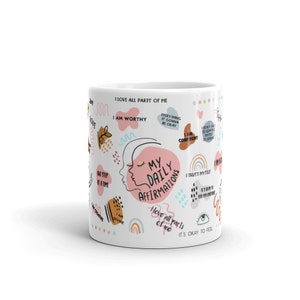 Puede incluir: Taza de cer&aacute;mica blanca con el texto "My Daily Affirmations" y varias afirmaciones positivas en un dise&ntilde;o colorido. La taza presenta ilustraciones de una cara, arco&iacute;ris y otros elementos decorativos.