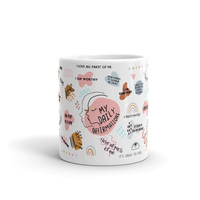 Puede incluir: Taza de cer&aacute;mica blanca con el texto "My Daily Affirmations" y varias afirmaciones positivas en un dise&ntilde;o colorido. La taza presenta ilustraciones de una cara, arco&iacute;ris y otros elementos decorativos.