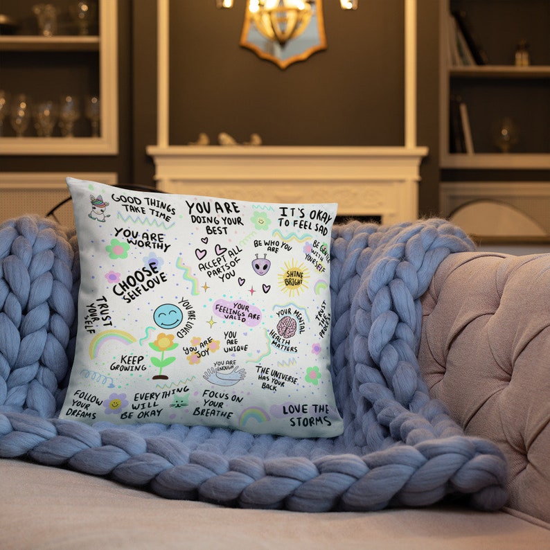 K&ouml;nnte beinhalten: Ein wei&szlig;es Kissen mit einem farbenfrohen Design mit positiven Affirmationen und Illustrationen. Das Kissen hat Text wie "You are worthy", "Choose self love", "Keep growing", "Follow your dreams", "Everything will be okay", "Focus on your breathe", "Love the storms", "It's okay to feel sad", "Be who you are", "Shine bright", "Your feelings are valid", "You are unique", "Your mental health matters", "The universe has your back".