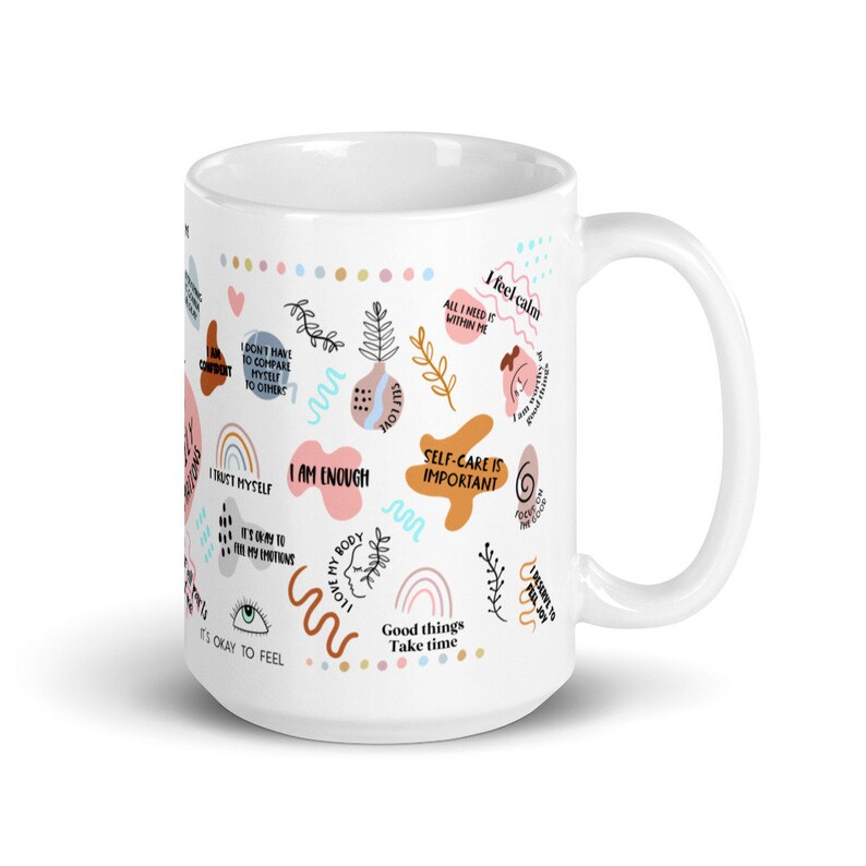 Puede incluir: Taza de cer&aacute;mica blanca con una variedad de texto y gr&aacute;ficos coloridos. La taza presenta frases como "Soy suficiente", "El autocuidado es importante" y "Est&aacute; bien sentir". El dise&ntilde;o incluye arco&iacute;ris, corazones y formas abstractas.