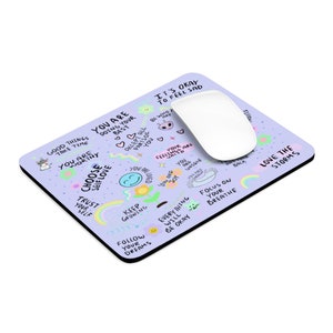 May include: A purple mouse pad with a variety of colorful, hand-drawn inspirational messages and illustrations. The text includes phrases like "Good Things Take Time", "You Are Worthy", "Choose Self Love", "Keep Growing", "Follow Your Dreams", "It's Okay To Feel Sad", "Love The Storms", and "Focus On Your Breathe".
