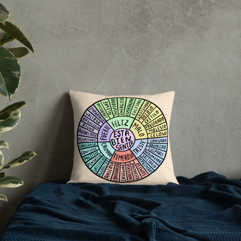 K&ouml;nnte beinhalten: Ein beiger Kissenbezug mit einem bunten Rad-Design. Das Rad hat die Worte "Feliz Esta Bien Sentir" in der Mitte. Die Worte um das Rad herum sind in Spanisch und beschreiben verschiedene Gef&uuml;hle.