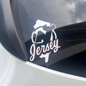May include: A white vinyl sticker with a red outline of the state of New Jersey and the text "Jersey" in a stylized font.
