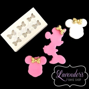 Op de afbeelding: Een siliconen mal met zes vlinder vormen en drie fondant uitsnijdingen van een cartoonfiguur met grote oren en een strik. Het figuur is roze en wit en heeft een gouden strik. De tekst "Lavender's Bake Shop" is zichtbaar in de afbeelding.