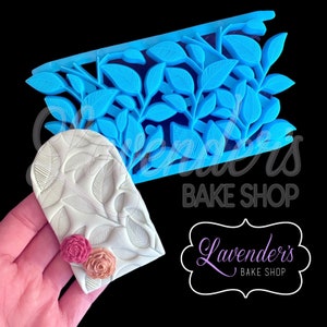 May include: A blue silicone mould with a leafy design. The mould is used to create a decorative cake border. A white fondant cake border with a leafy design is shown next to the mould.