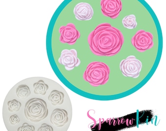 Può includere: Stampo in silicone con nove cavità a forma di rosa. Lo stampo è bianco e ha una superficie liscia. Lo stampo è circondato da un cerchio verde con rose rosa e bianche.