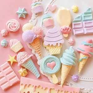 Puede incluir: Surtido de conos de helado, cupcakes, piruletas y barras de chocolate de color pastel. Los art&iacute;culos est&aacute;n dispuestos sobre una superficie blanca con un fondo rosa.