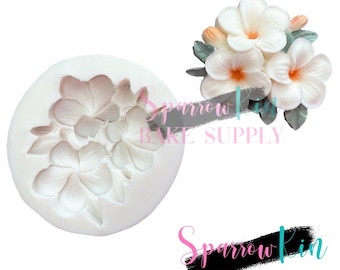 Può includere: Uno stampo in silicone bianco con un design di un gruppo di fiori bianchi. Lo stampo viene utilizzato per realizzare decorazioni per torte.