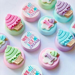 Puede incluir: Surtido de galletas decoradas con tem&aacute;tica de cono de helado. Las galletas presentan diferentes colores y dise&ntilde;os, incluyendo rosa, azul, verde y morado. Algunas galletas tienen el texto "We all scream for ice cream" impreso en ellas.