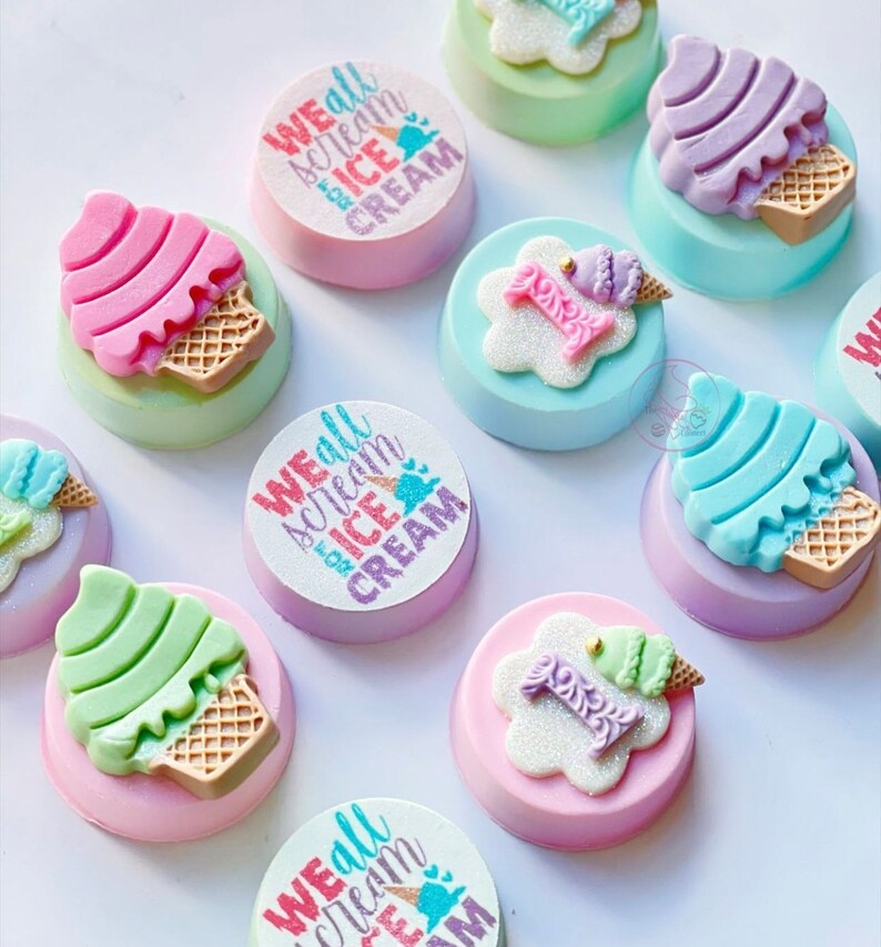 Puede incluir: Surtido de galletas decoradas con tem&aacute;tica de cono de helado. Las galletas presentan diferentes colores y dise&ntilde;os, incluyendo rosa, azul, verde y morado. Algunas galletas tienen el texto "We all scream for ice cream" impreso en ellas.