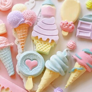 Puede incluir: Una colecci&oacute;n de conos de helado en miniatura, paletas y piruletas de colores. Los conos de helado est&aacute;n decorados con chispas y tienen bolas de helado de diferentes colores. Las paletas tienen forma de coraz&oacute;n y estrella. Las piruletas son redondas y tienen un dise&ntilde;o de coraz&oacute;n.