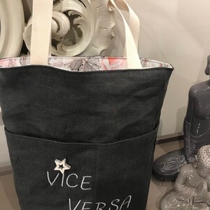 Può includere: Una borsa tote in tela nera con una stella bianca e il testo "VICE VERSA" ricamato sul davanti. La borsa ha una fodera bianca e due manici bianchi.