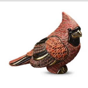 May include: A detailed, carved wooden cardinal figurine. The bird features a red body, black accents, and gold-colored beak and wing details. The carving showcases intricate patterns and textures, creating a lifelike representation of the bird.