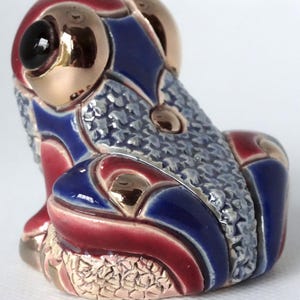 May include: A ceramic frog figurine with a blue, red, and gold patterned design. The frog is sitting with its legs tucked underneath its body.