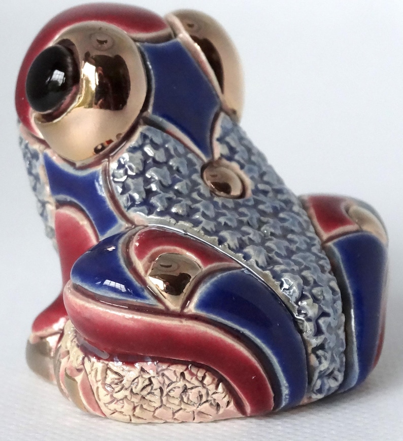 May include: A ceramic frog figurine with a blue, red, and gold patterned design. The frog is sitting with its legs tucked underneath its body.