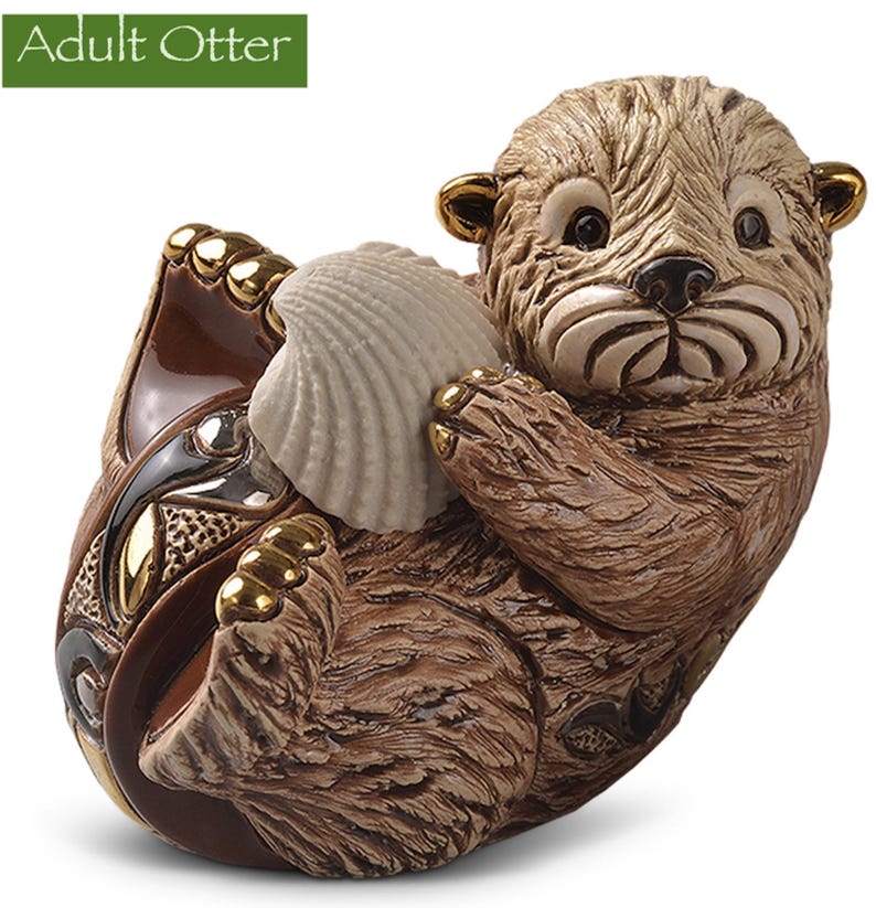 May include: A ceramic figurine of an adult otter holding a seashell. The otter is brown and has a white belly. The seashell is white and has a brown interior. The figurine is sitting on a brown base with gold accents.