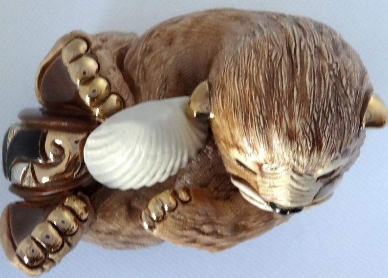 May include: A ceramic figurine of a brown bear holding a white seashell. The bear has gold accents on its paws and ears.