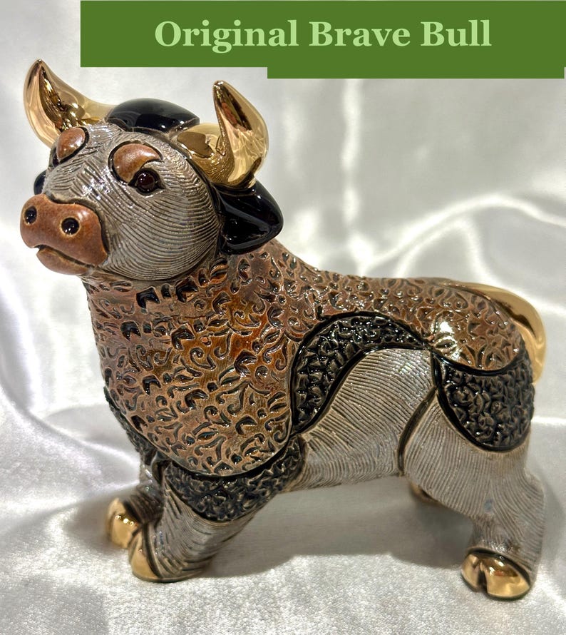 May include: A ceramic bull figurine featuring a textured brown and silver body with intricate swirling patterns. The bull has polished gold-colored horns and hooves, with black accents on the head and flanks. The text Original Brave Bull is visible.