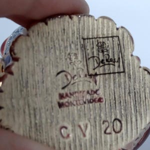 May include: Close-up of the bottom of a ceramic figurine. The figurine is signed "De Rossi" and "Handmade in Montevideo". The number "CV 20" is also visible.