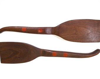 May include: Two wooden spatulas with red accents. The spatulas are made of dark wood and have a long handle with a rounded end. The spatulas are perfect for cooking and serving.